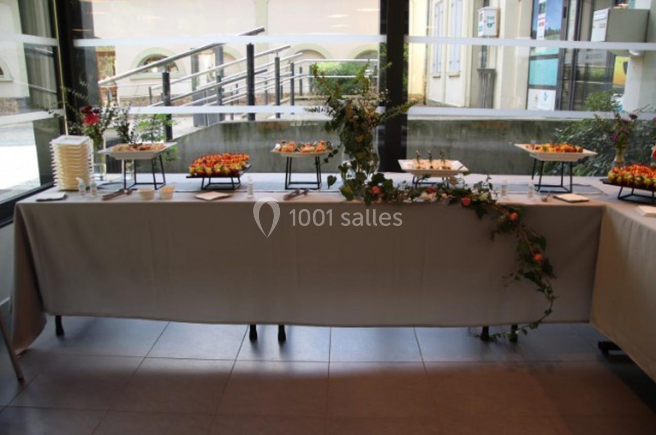 Buffet dressé avec des plateaux de verrines et d'amuse-bouches, décoré de feuillage, dans une salle lumineuse.