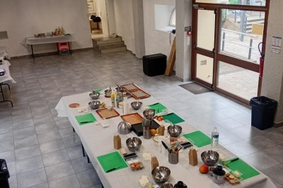 Tables dressées avec des ustensiles de cuisine, planches vertes et ingrédients, dans une salle lumineuse.