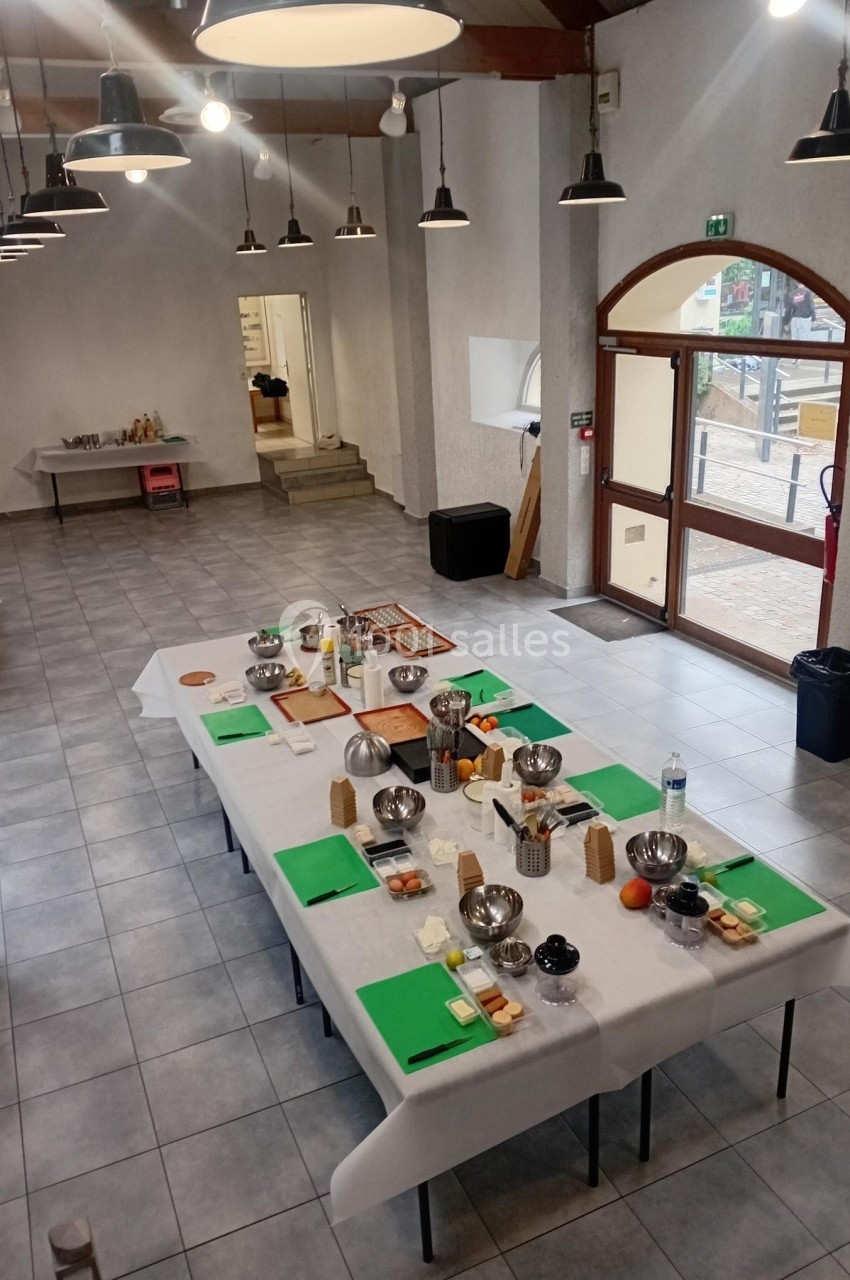 Salle lumineuse avec des tables dressées pour un atelier culinaire, comprenant ustensiles, ingrédients et planches de…