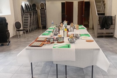 Tables dressées avec des ustensiles de cuisine, planches vertes et ingrédients, dans une salle lumineuse.