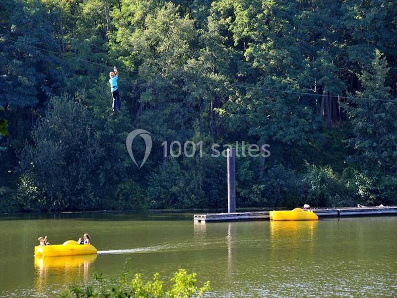 Une personne glisse sur une tyrolienne au-dessus d'un lac, tandis que des pédalos jaunes flottent sur l'eau.