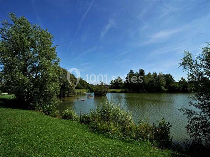 Vue d'un lac entouré de verdure et d'arbres sous un ciel bleu dégagé.
