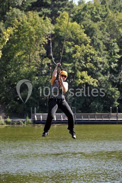 Une personne descend en tyrolienne au-dessus d'un plan d'eau entouré d'arbres.