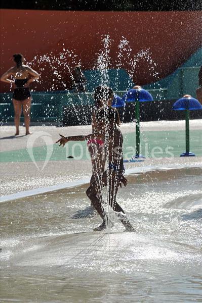 Deux enfants jouent dans des jets d'eau d'une aire de jeux aquatique par une journée ensoleillée.