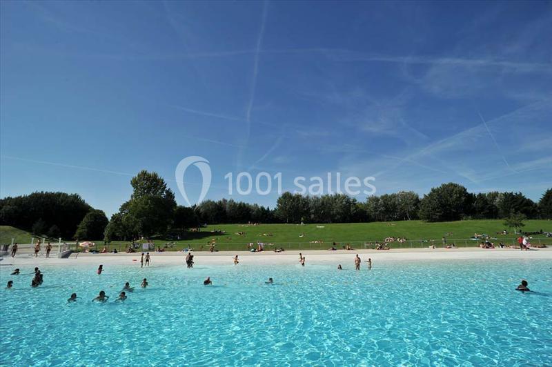 Des personnes se baignent dans une piscine extérieure entourée d'une pelouse et d'arbres sous un ciel dégagé.