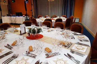 Salle de réception avec tables rondes dressées, nappes blanches, chaises rouges et décorations de ballons colorés.
