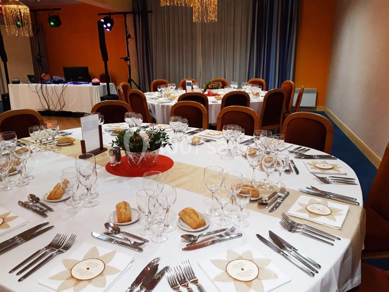 Salle de réception avec tables rondes dressées, nappes blanches, couverts, verres et décorations florales.