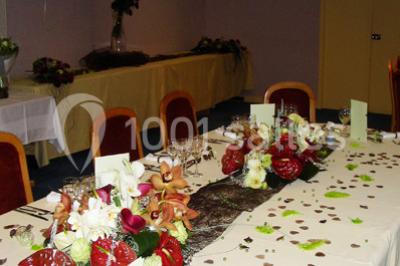 Salle de réception avec tables rondes dressées, nappes blanches, chaises rouges et décorations de ballons colorés.