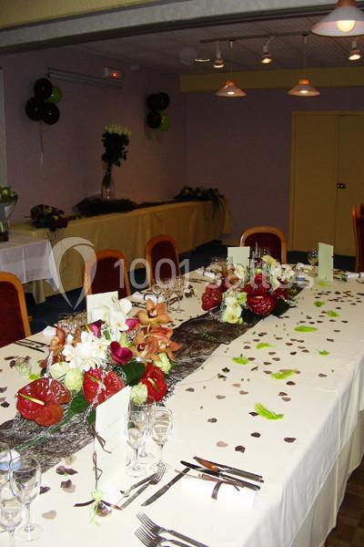 Salle décorée pour un repas festif avec une grande table ornée de fleurs, pétales et menus, éclairée par des suspensions.