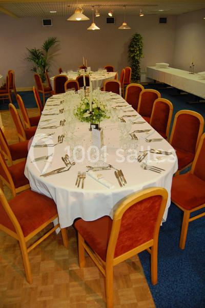 Table dressée pour un repas formel, avec nappes blanches, vaisselle élégante et chaises en bois rembourrées.