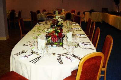 Salle de réception avec tables rondes dressées, nappes blanches, chaises rouges et décorations de ballons colorés.