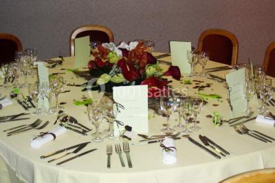 Salle de réception avec tables rondes dressées, nappes blanches, chaises rouges et décorations de ballons colorés.