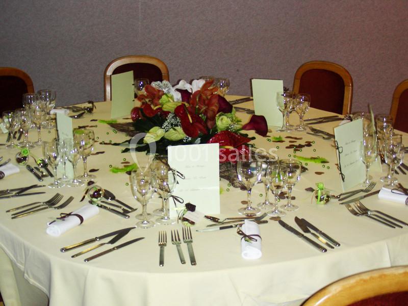 Table ronde dressée avec nappes blanches, couverts, verres, menus et centre de table floral coloré.