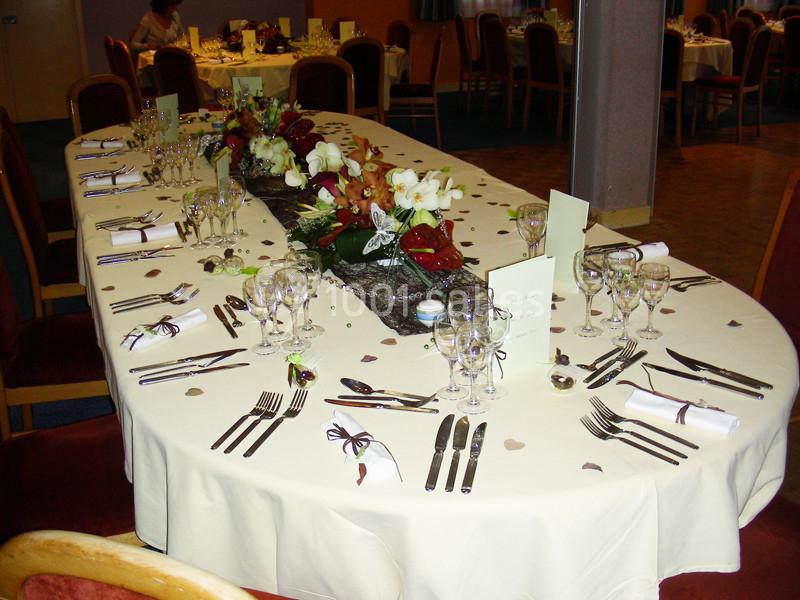 Table élégamment dressée avec nappes blanches, couverts, verres et centre de table floral dans une salle de réception.