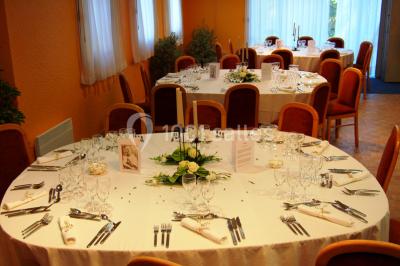 Salle de réception avec tables rondes dressées, nappes blanches, chaises rouges et décorations de ballons colorés.