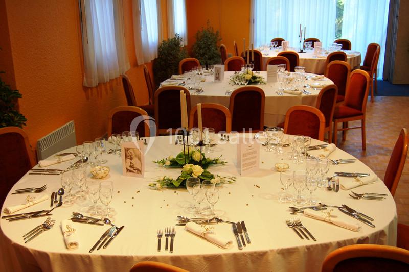 Salle de réception avec tables rondes dressées, nappes blanches, décorations florales et couverts disposés.