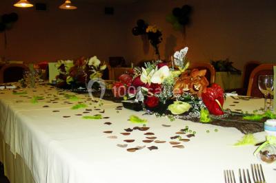 Salle de réception avec tables rondes dressées, nappes blanches, chaises rouges et décorations de ballons colorés.