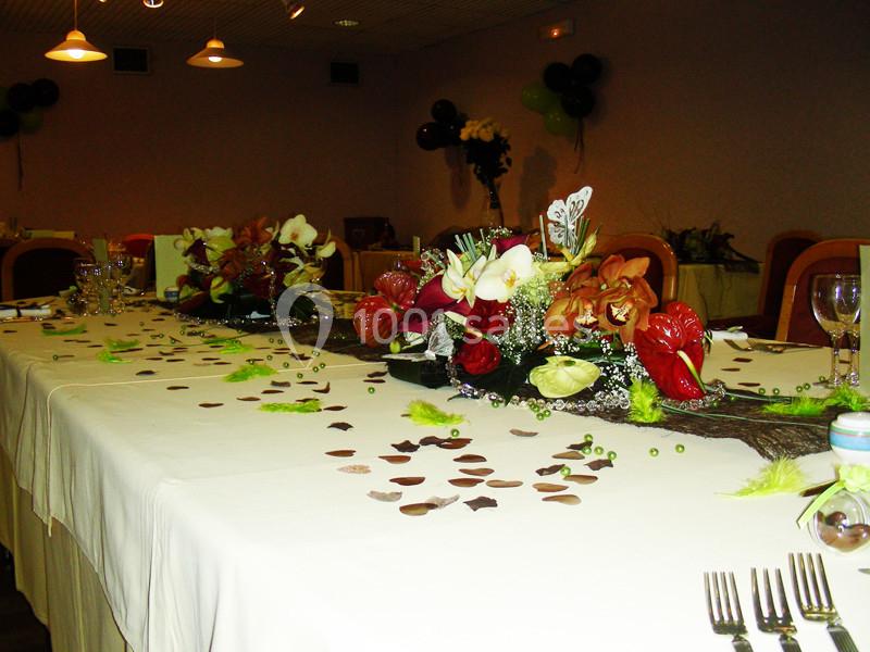 Table décorée avec des fleurs colorées, des confettis et des éléments verts, dans une salle éclairée pour un événement.