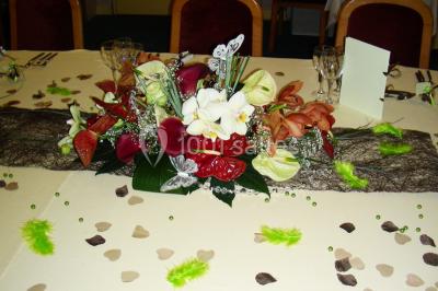 Salle de réception avec tables rondes dressées, nappes blanches, chaises rouges et décorations de ballons colorés.