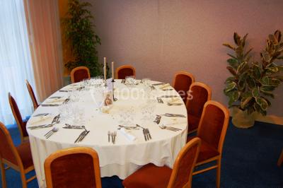 Salle de réception avec tables rondes dressées, nappes blanches, chaises rouges et décorations de ballons colorés.