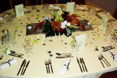 Salle de réception avec tables rondes dressées, nappes blanches, chaises rouges et décorations de ballons colorés.
