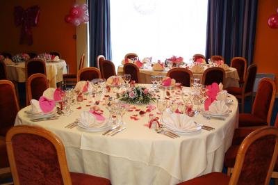 Salle de réception avec tables rondes dressées, nappes blanches, chaises rouges et décorations de ballons colorés.