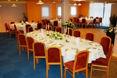 Salle de réception avec tables rondes dressées, nappes blanches, chaises rouges et décorations de ballons colorés.