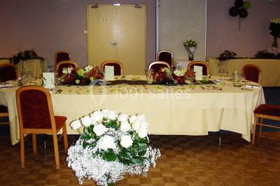 Salle de réception avec tables rondes dressées, nappes blanches, chaises rouges et décorations de ballons colorés.
