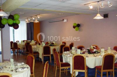 Salle de réception avec tables rondes dressées, nappes blanches, chaises rouges et décorations de ballons colorés.