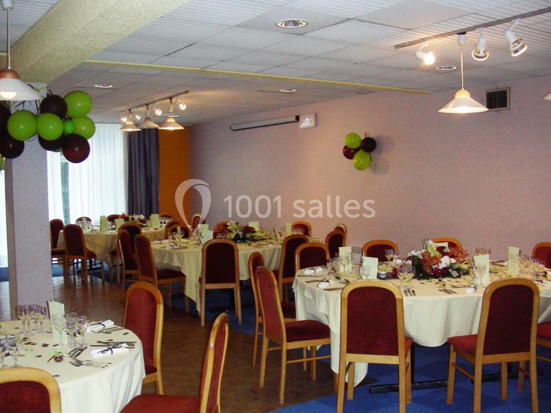 Salle de réception avec tables rondes dressées, nappes blanches, chaises rouges et décorations de ballons colorés.