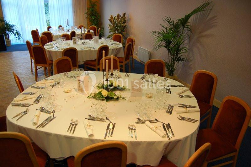 Salle de réception avec tables rondes dressées, nappes blanches, couverts, bougies et décorations florales.