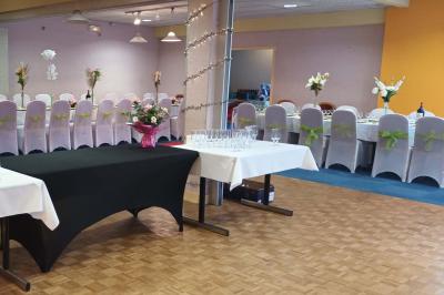 Salle de réception avec tables rondes dressées, nappes blanches, chaises rouges et décorations de ballons colorés.