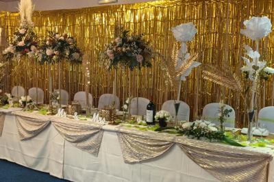 Salle de réception avec tables rondes dressées, nappes blanches, chaises rouges et décorations de ballons colorés.