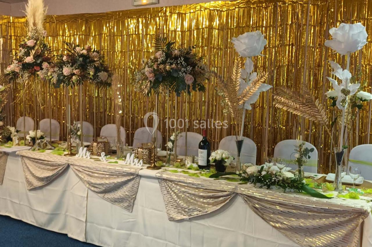 Table de réception décorée avec des fleurs, des feuilles dorées et une nappe blanche devant un fond scintillant doré.