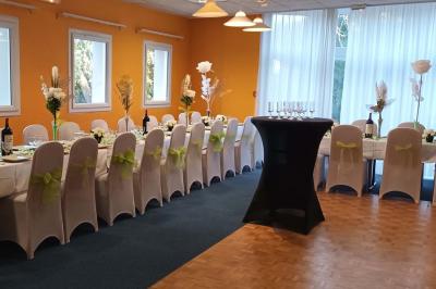 Salle de réception avec tables rondes dressées, nappes blanches, chaises rouges et décorations de ballons colorés.