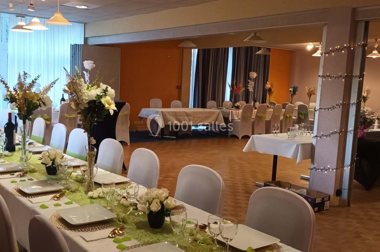 Salle de réception décorée avec des tables dressées, nappes blanches, centres de table fleuris et guirlandes lumineuses.