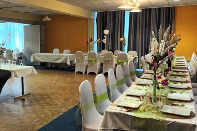 Salle de réception avec tables rondes dressées, nappes blanches, chaises rouges et décorations de ballons colorés.