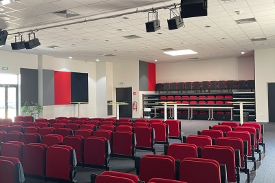 Salle de réunion lumineuse avec des tables disposées en U, des chaises grises et un tableau blanc au fond.