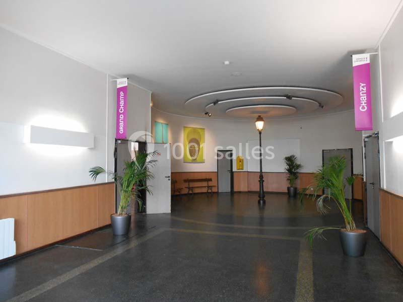 Hall spacieux avec sol sombre, murs clairs, plantes en pot, lampadaire central et panneaux suspendus indiquant ’Chanzy’.