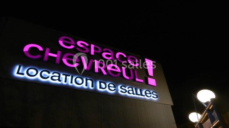 Enseigne lumineuse indiquant ’Espace Chevreul, Location de salles’ sur un bâtiment, vue de nuit.