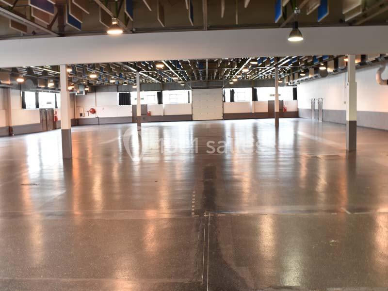 Vue d'un grand espace intérieur vide avec sol en béton poli, colonnes et plafond industriel.