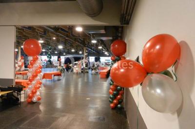 Salle vide avec sol noir, murs blancs et gris, éclairage au plafond, plante en pot et porte métallique au fond.