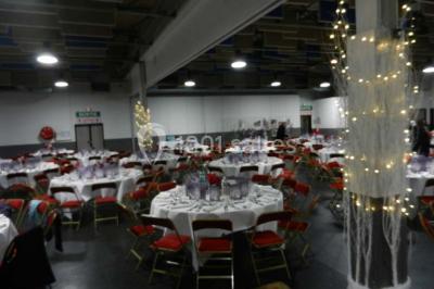 Salle vide avec sol noir, murs blancs et gris, éclairage au plafond, plante en pot et porte métallique au fond.
