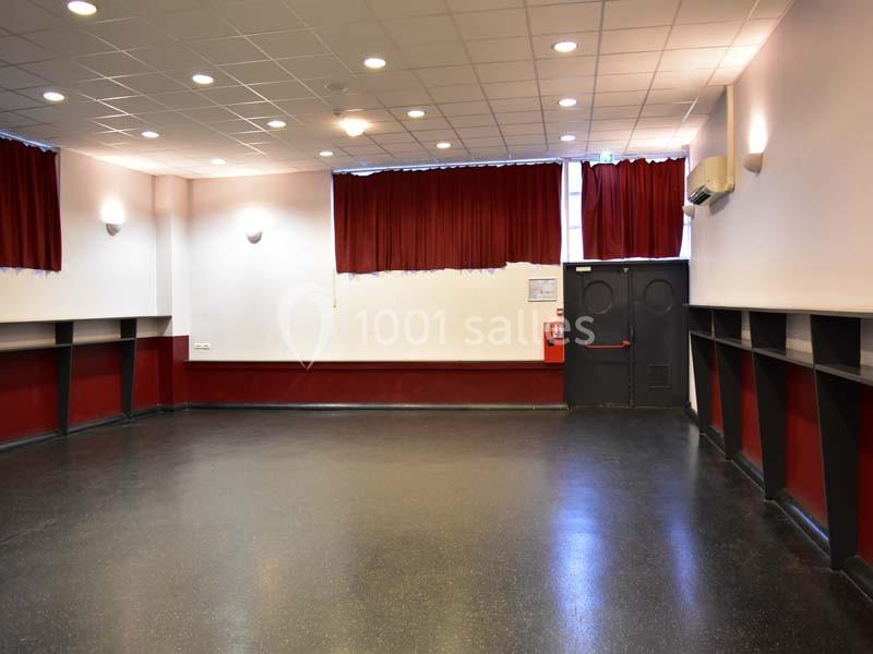 Salle vide avec sol noir, murs rouges et blancs, rideaux rouges, éclairage au plafond et porte double au fond.