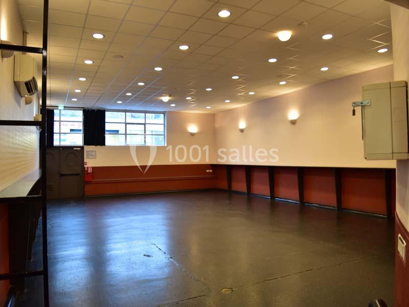 Salle vide avec sol sombre, murs clairs, plafond à dalles blanches et éclairage encastré, fenêtre et porte au fond.