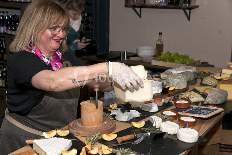 Une femme prépare un plateau de fromages variés sur un comptoir, avec des décorations et des étiquettes.
