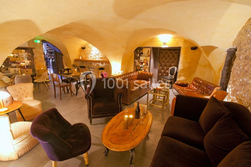 Salon voûté avec murs en pierre, mobilier vintage, canapés en cuir et éclairage chaleureux.