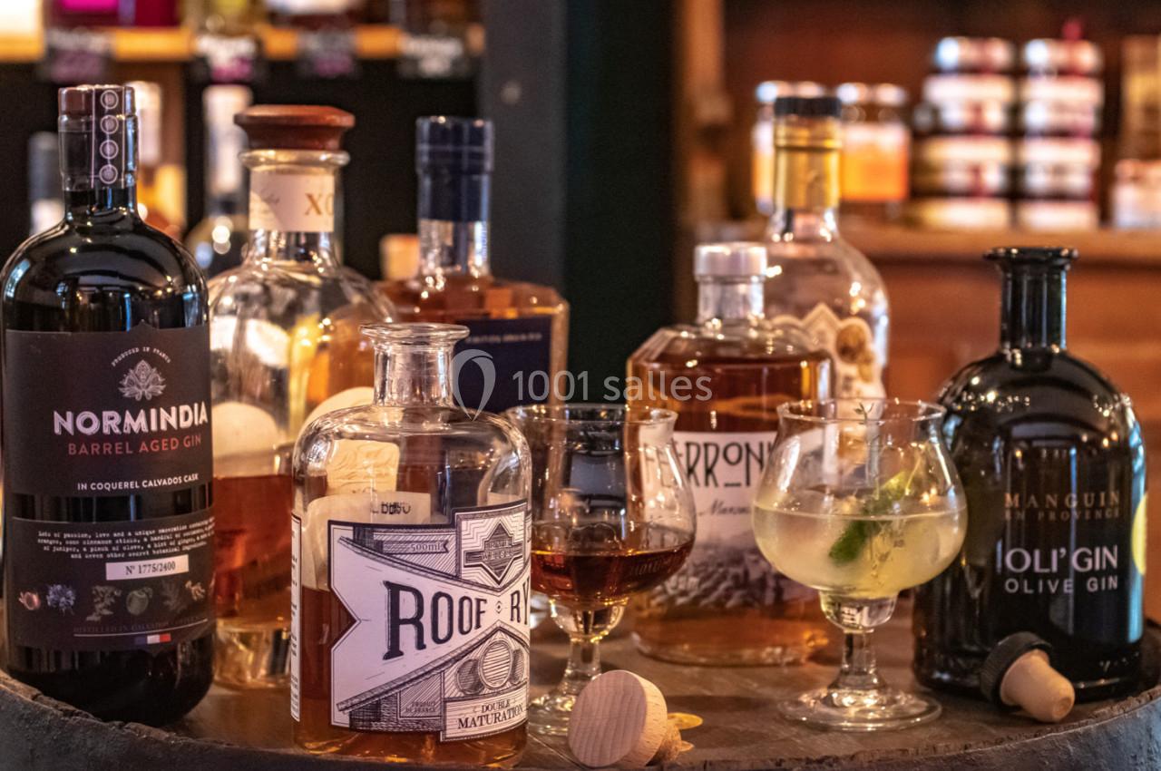 Bouteilles de spiritueux variés et verres servis sur un tonneau dans un cadre chaleureux de bar ou cave.