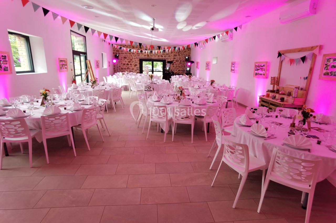 Salle décorée pour un événement avec tables rondes dressées, guirlandes colorées et éclairage rose.
