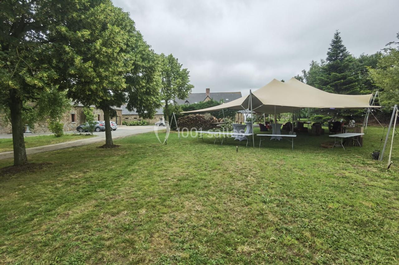 Tente beige installée sur une pelouse avec des tables dressées, entourée d'arbres et de bâtiments en arrière-plan.